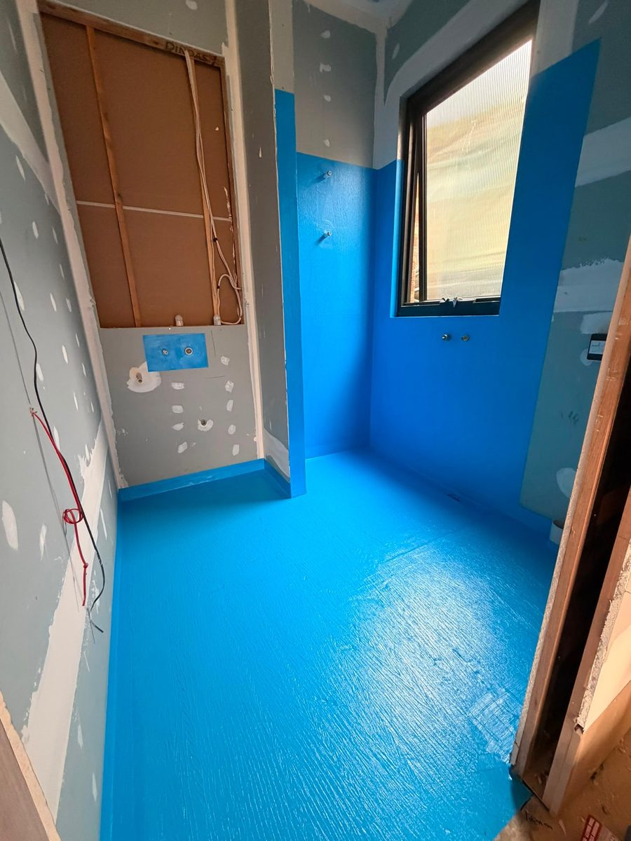 Bathroom mid-build with blue waterproofing membrane applied to the floor and lower walls — photo by Brady Tiling with Fliese Imports